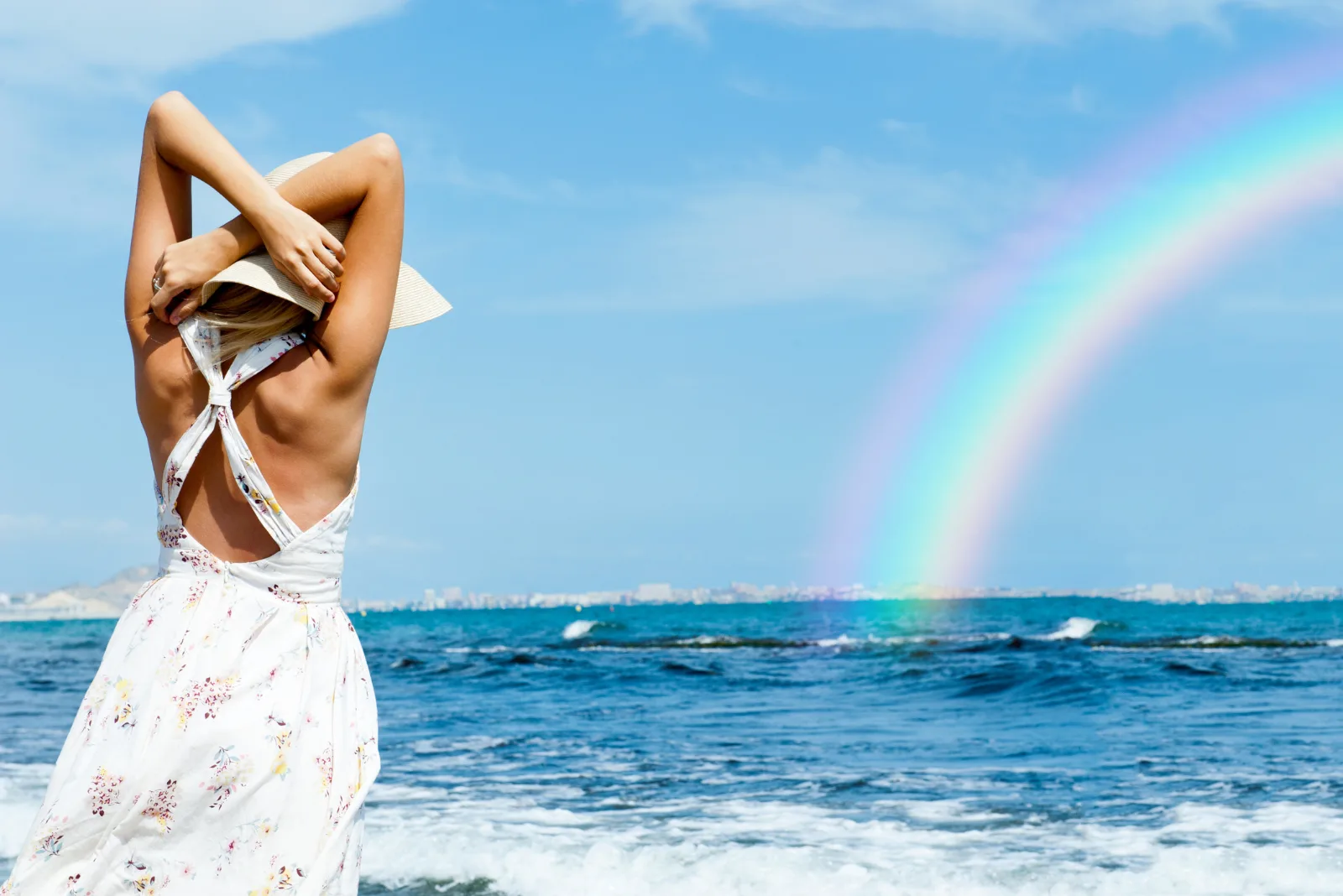 Eine Frau steht am Strand und betrachtet den Regenbogen