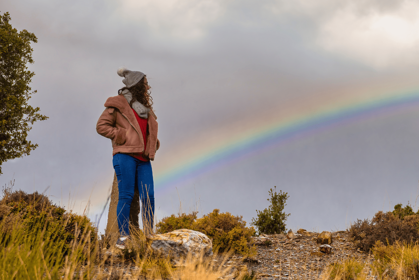 Eine Frau steht auf einem Berg und betrachtet den Regenbogen