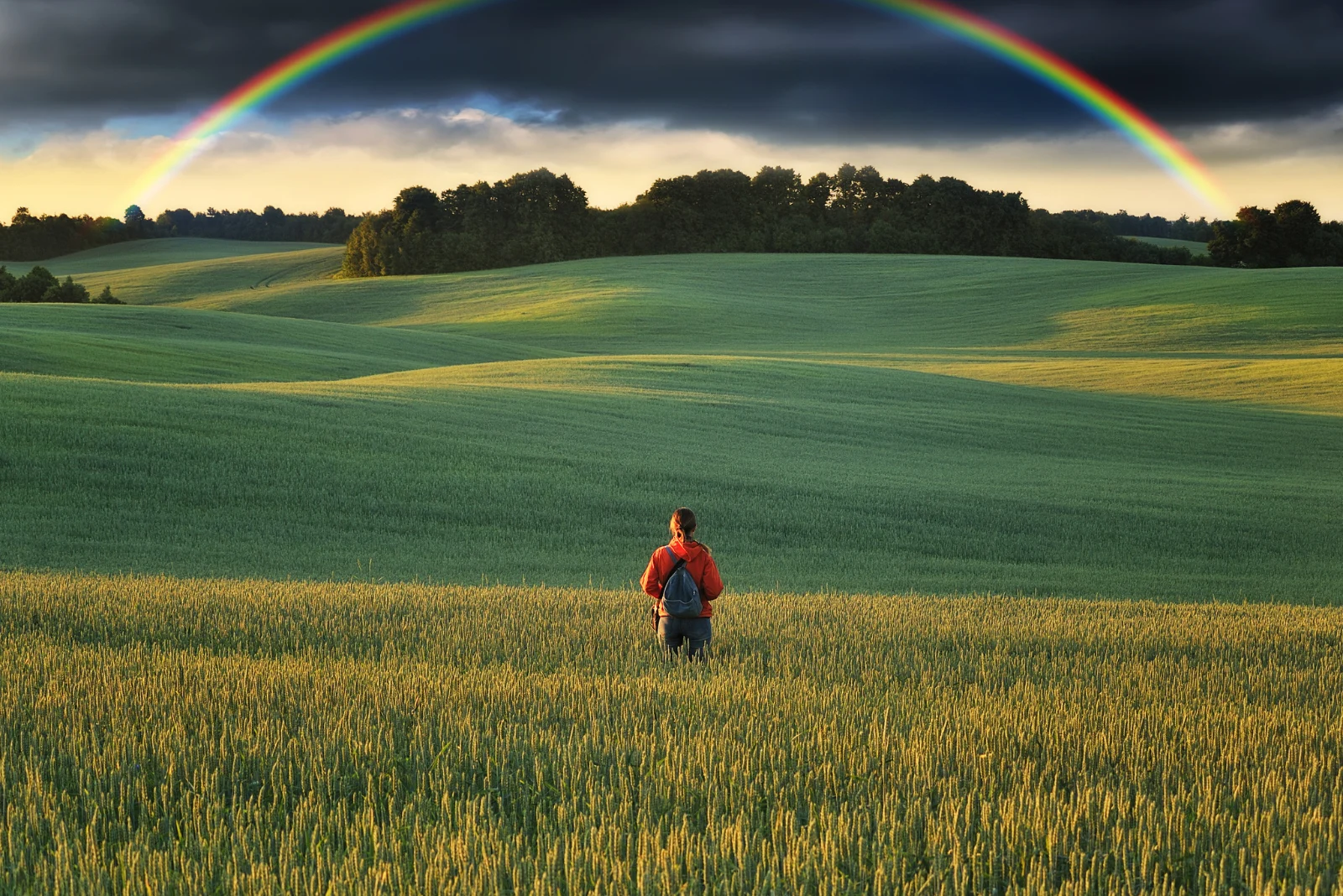 Eine Frau steht auf einem Feld und betrachtet einen Regenbogen