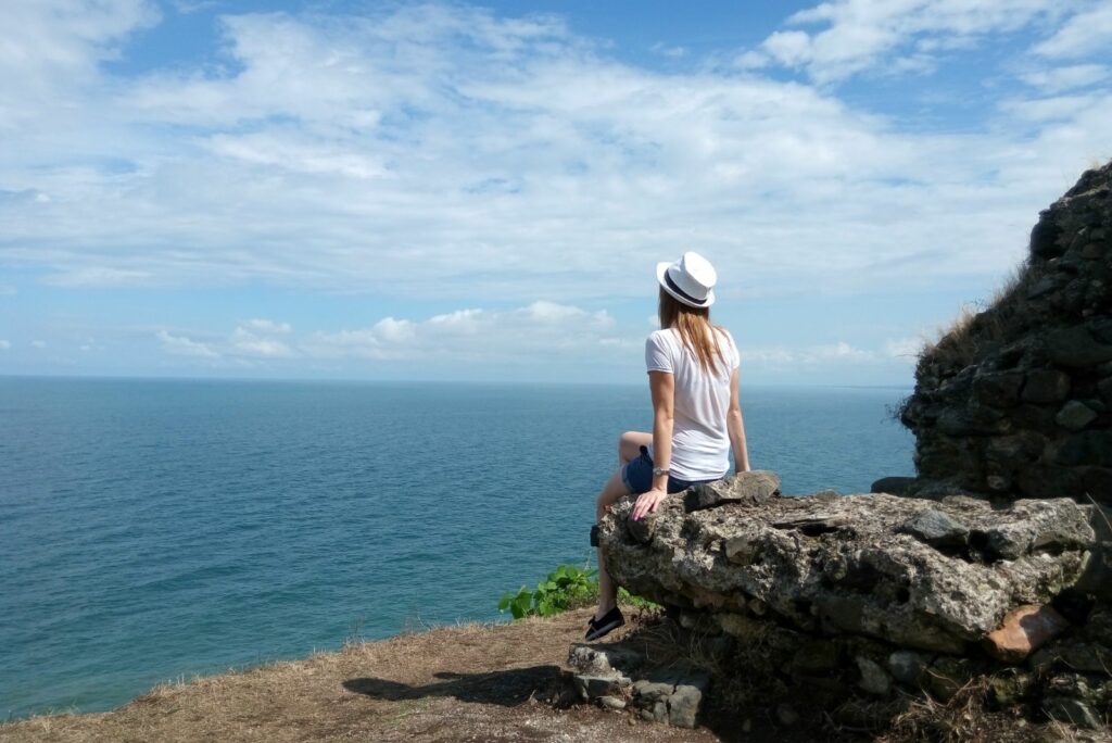 Ein Mädchen sitzt auf einem Felsen und blickt auf das Meer