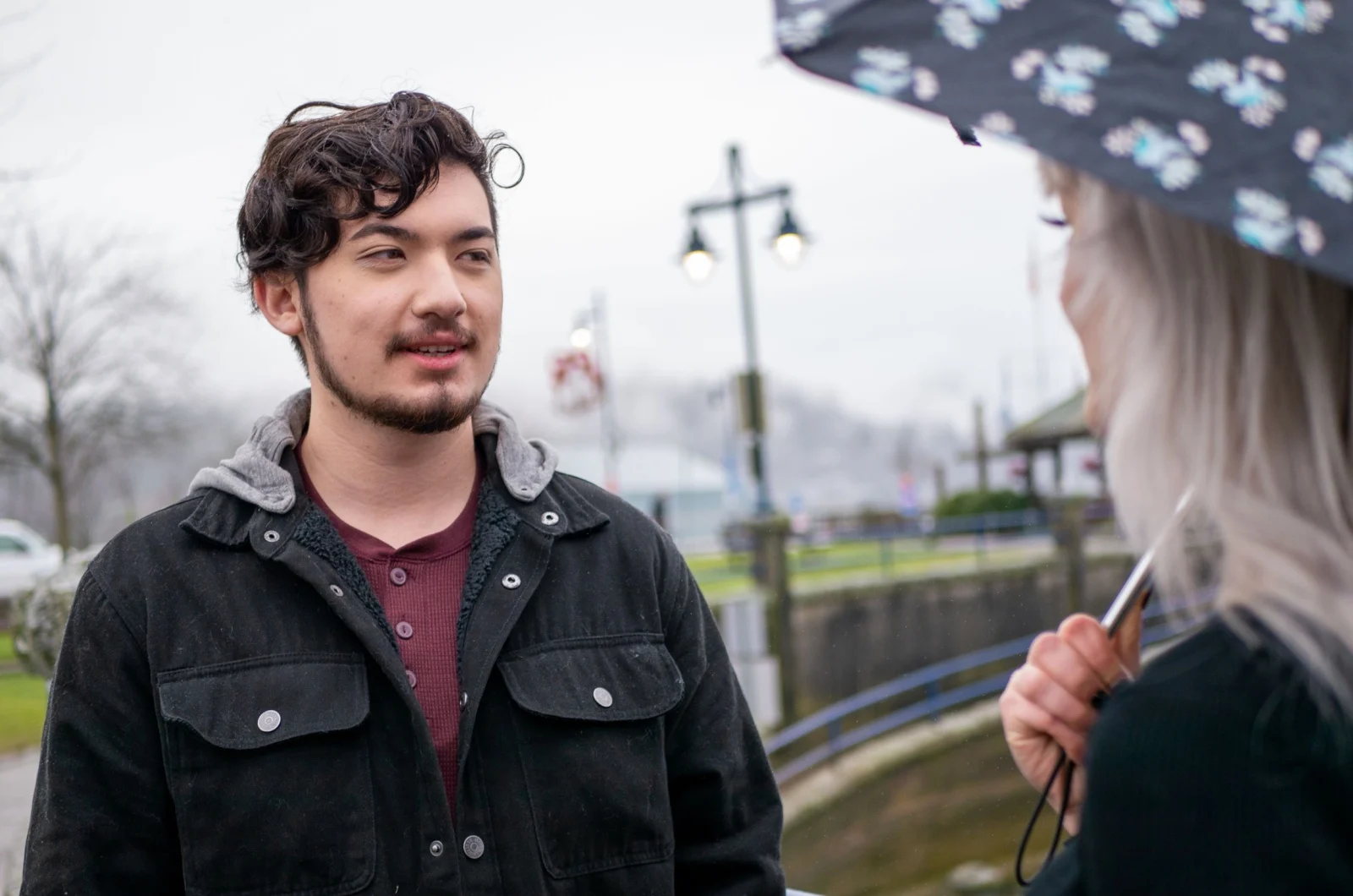 Frau haelt einen Regenschirm und spricht mit einem Mann