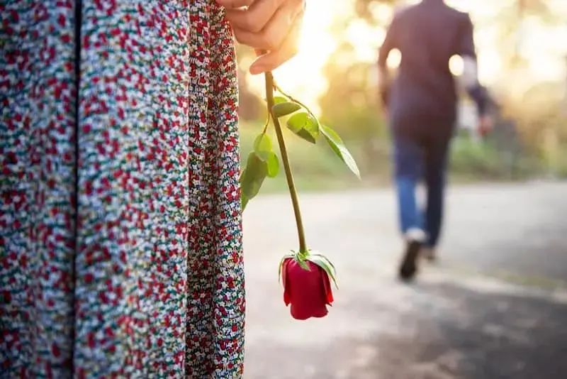 Frau mit Rose steht und schaut, wie viele Blätter