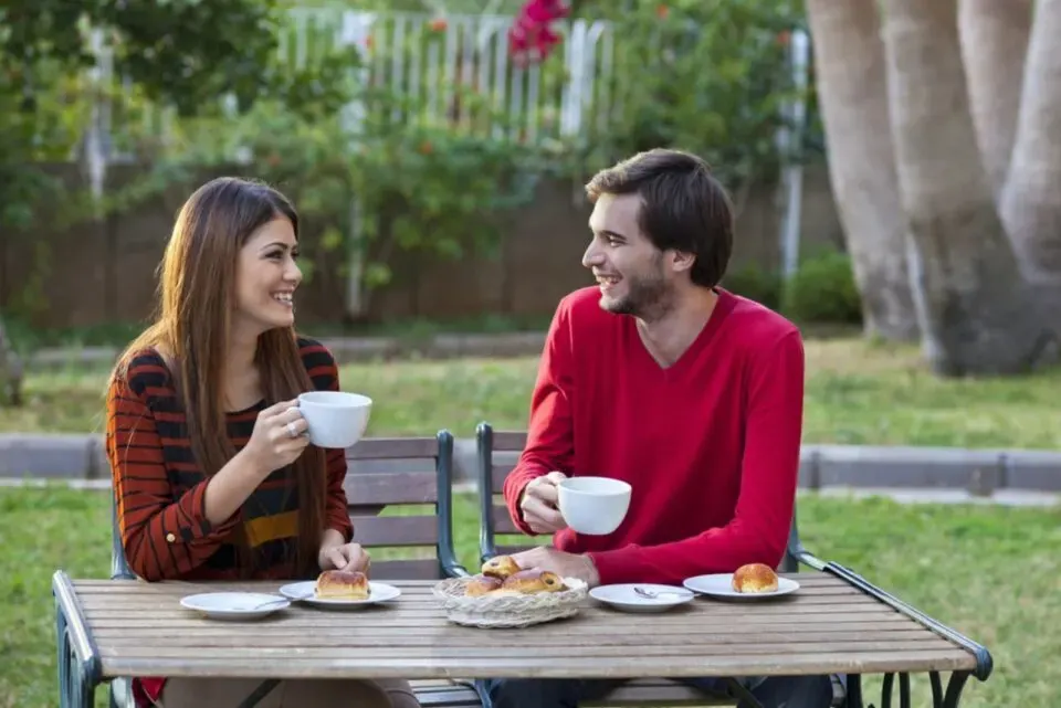 Laechelnder Mann und Frau, die draussen sitzen und sich beim Kaffee unterhalten