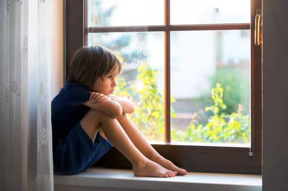 Trauriger Junge, der am Fenster sitzt