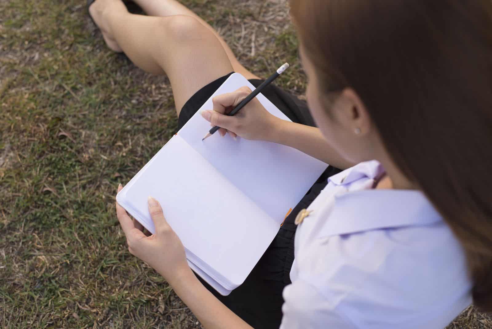 Eine Frau sitzt im Gras und schreibt einen Brief