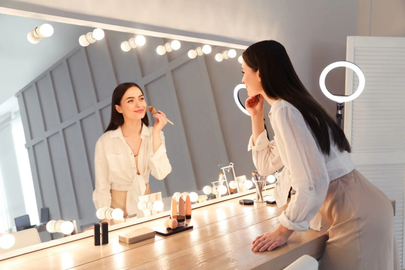 Eine Frau steht neben einem Spiegel und trägt Make-up auf