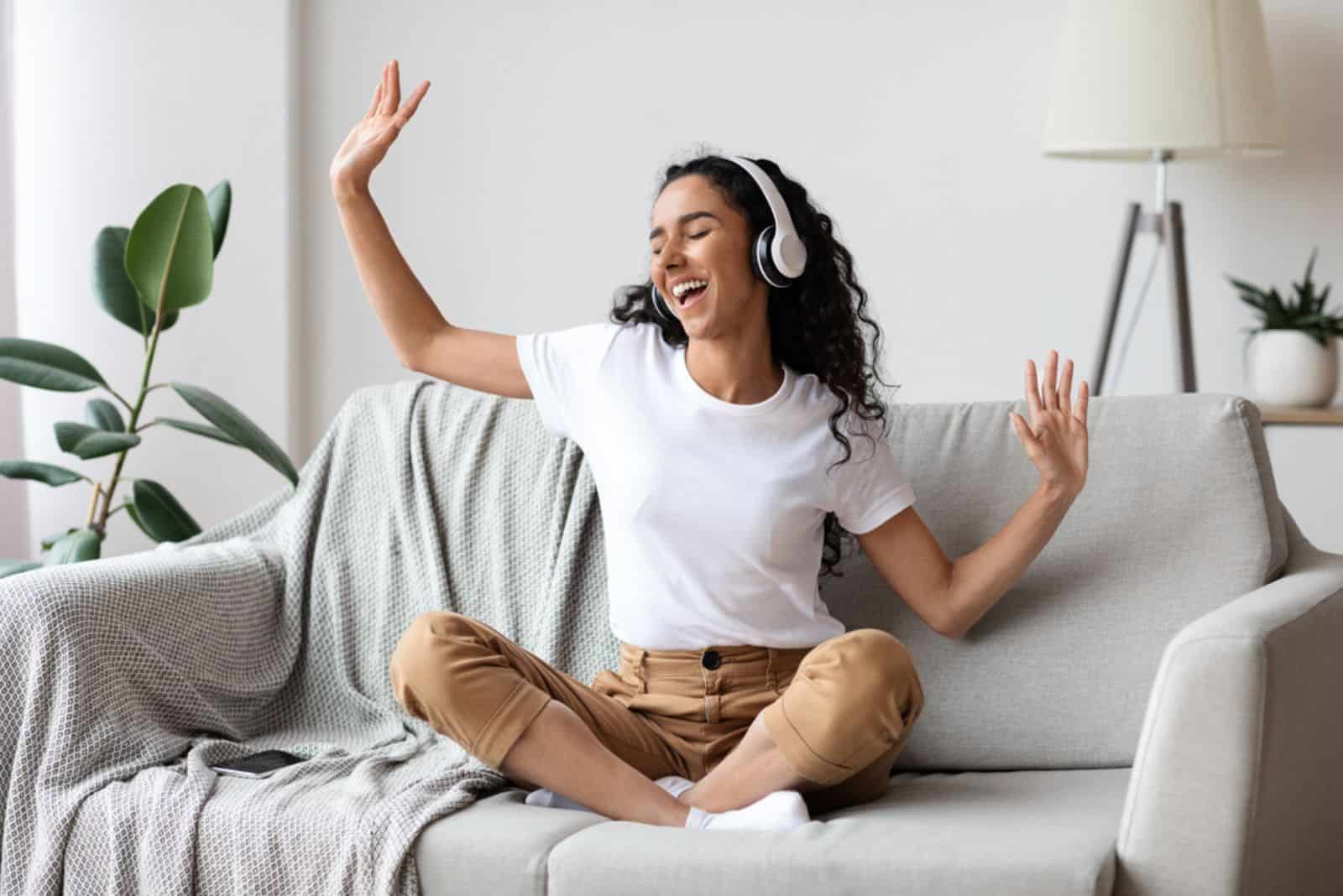 Lächelndes Mädchen sitzt auf der Couch und tanzt mit Kopfhörern in den Ohren