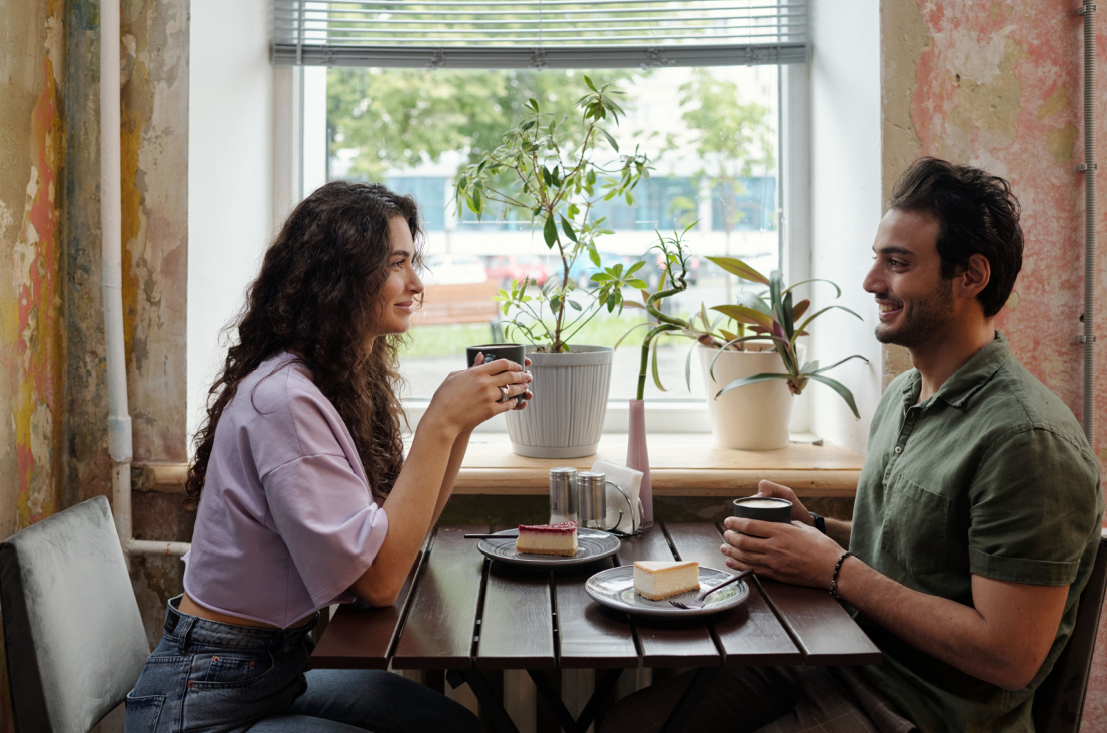 Junge Frau und ihr lächelnder Freund sitzen mit einer Tasse Kaffee am Tisch