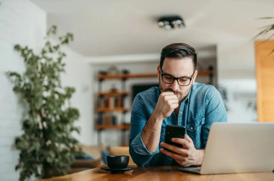 Mann sitzt und haelt Telefon