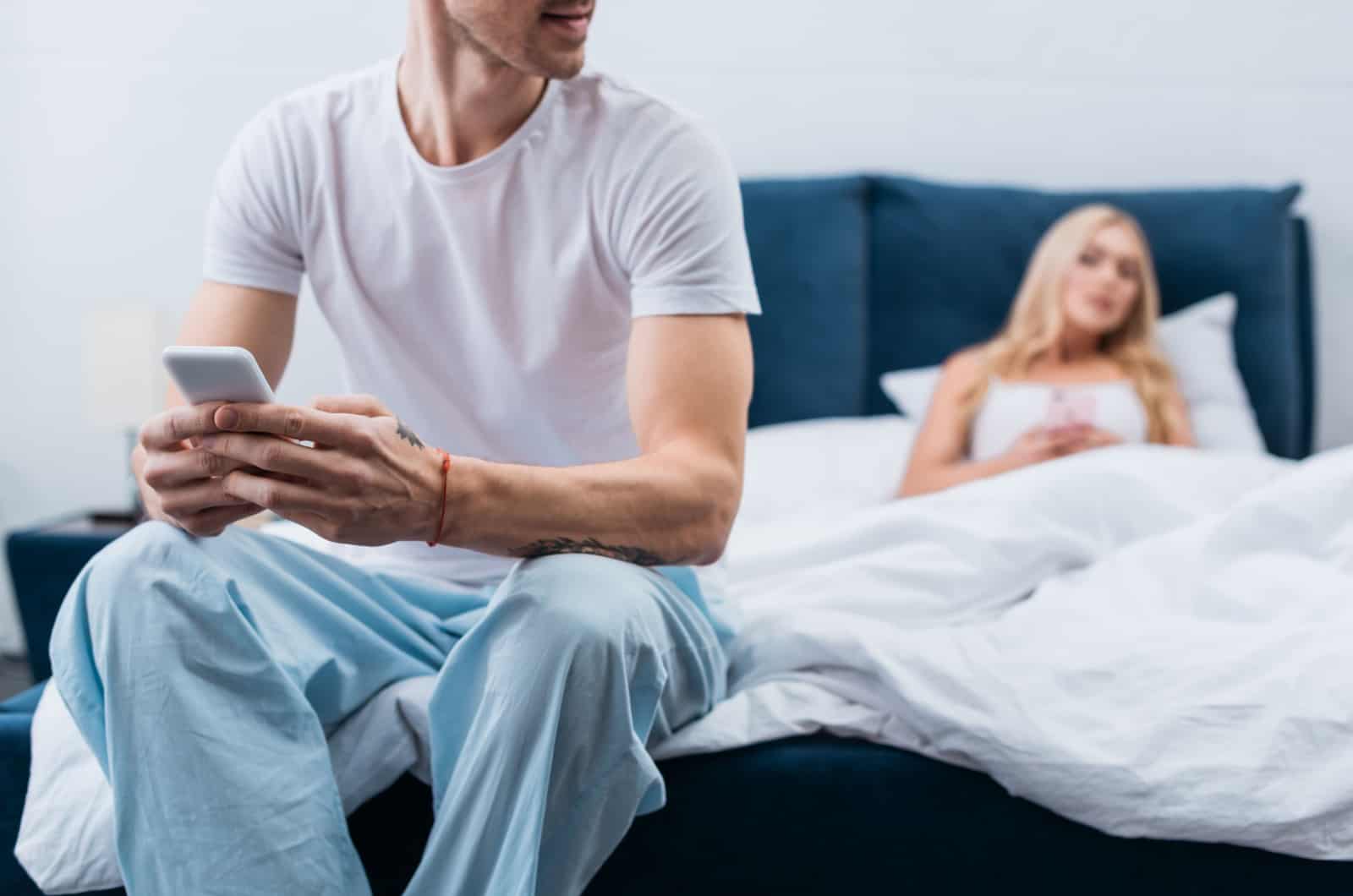 Junger Mann im Schlafanzug mit Smartphone im Bett