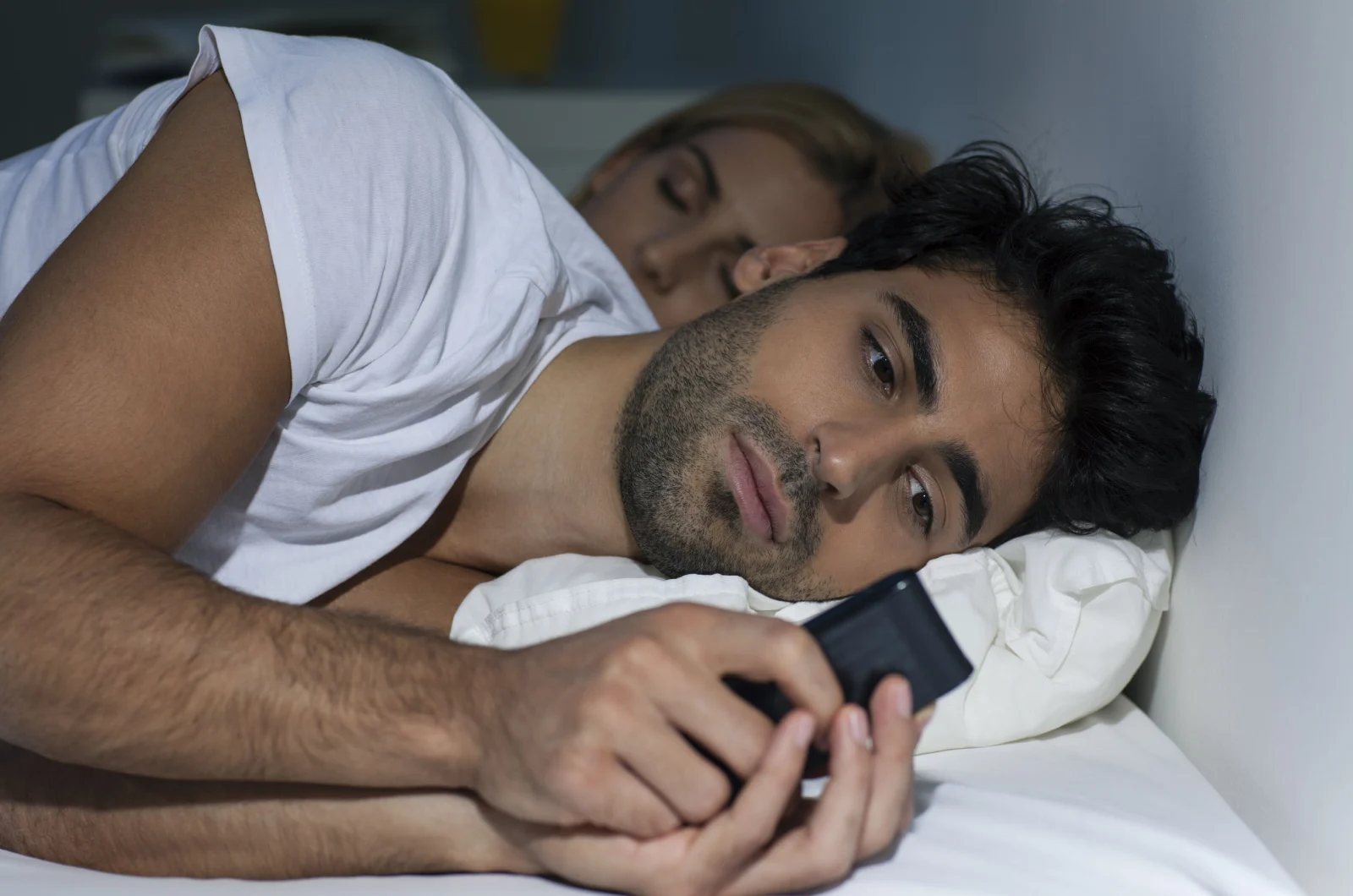 Mann tippt am Telefon, während Frau schläft