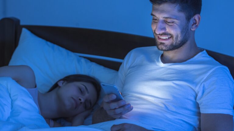 mann am handy neben schlafender frau