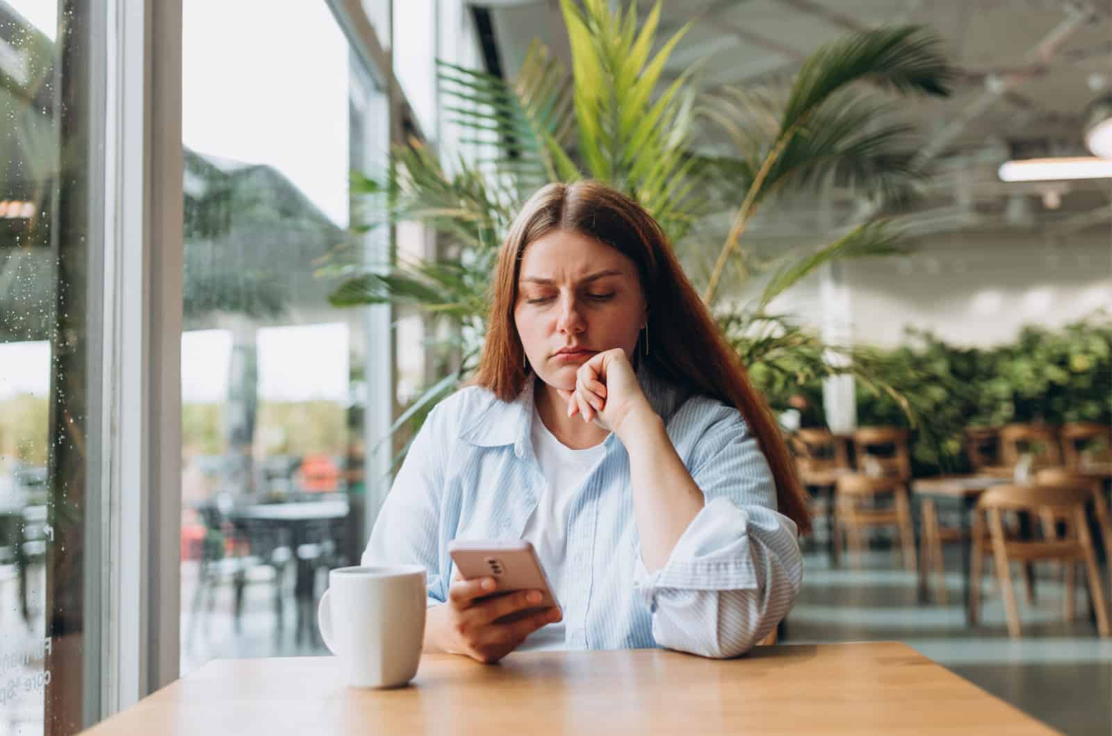 Traurige junge Frau in einem Café, die auf ihr Smartphone schaut
