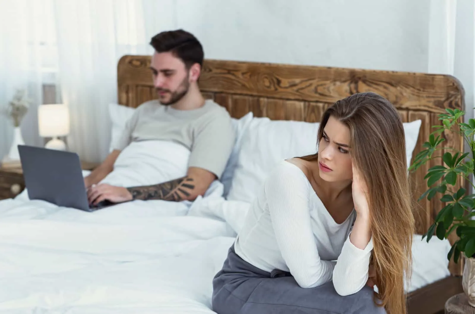 Verärgerte Frau sitzt auf dem Bett und schaut ihren Mann an