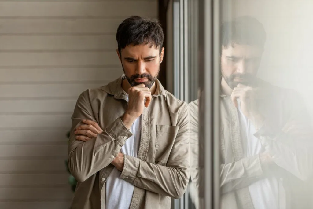 nachdenklicher mann der am fenster lehnt