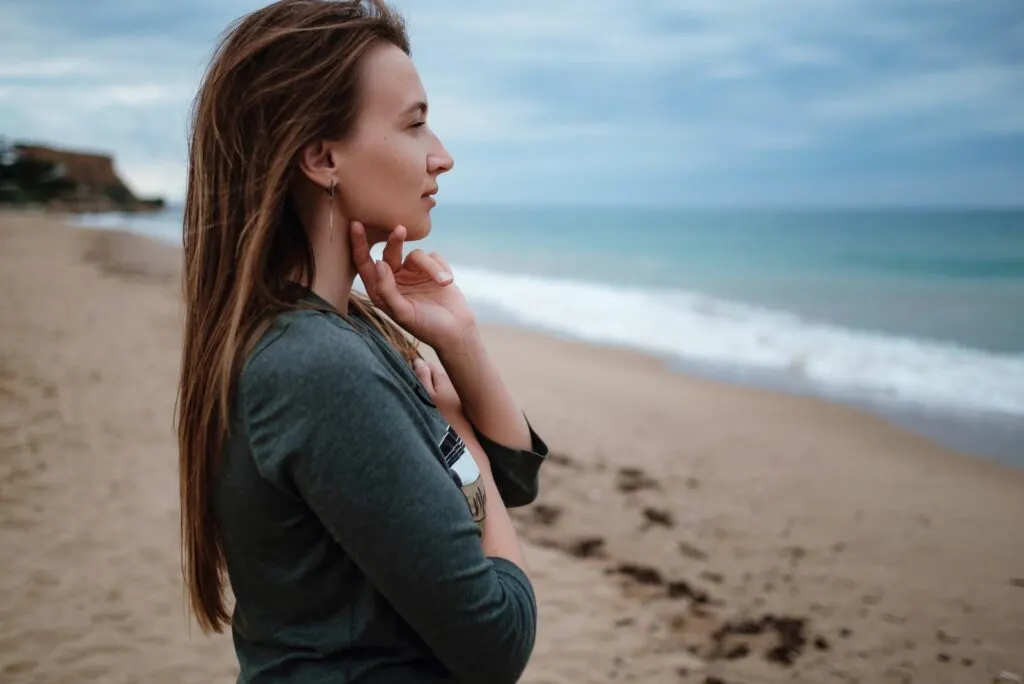 Ein Maedchen mit langen braunen Haaren steht am Strand