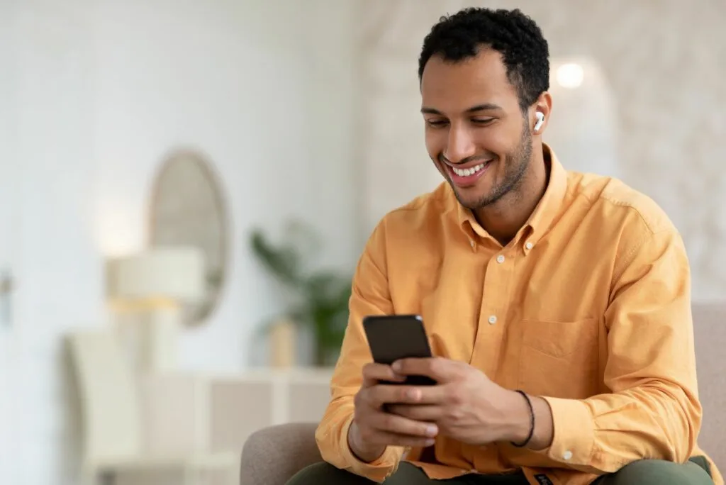 Ein Mann mit Kopfhoerern in den Ohren haelt ein Mobiltelefon in der Hand