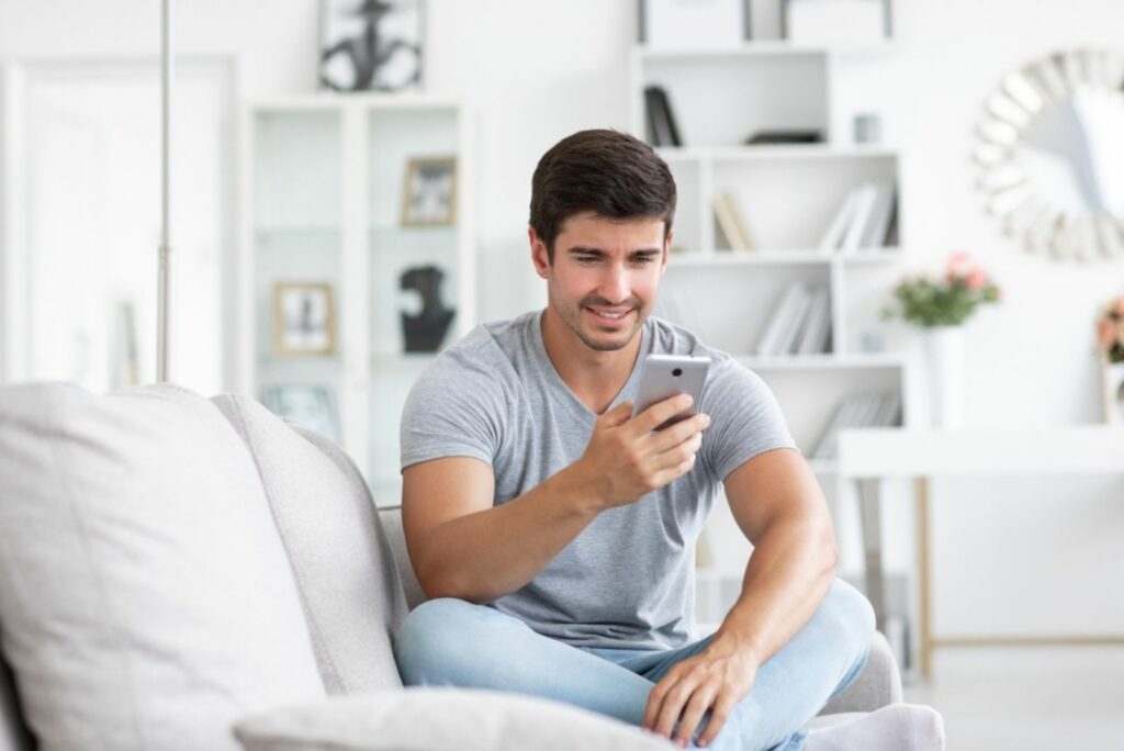 Ein Mann sitzt auf der Couch, tippt am Telefon und lacht