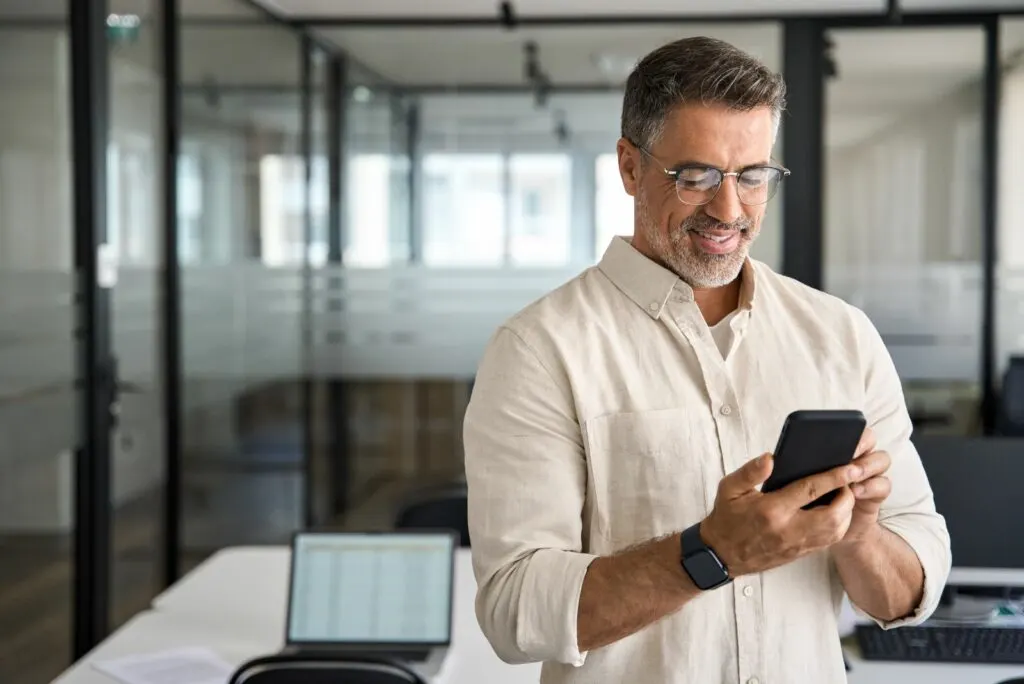 Ein Mann steht im Buero und tippt am Telefon