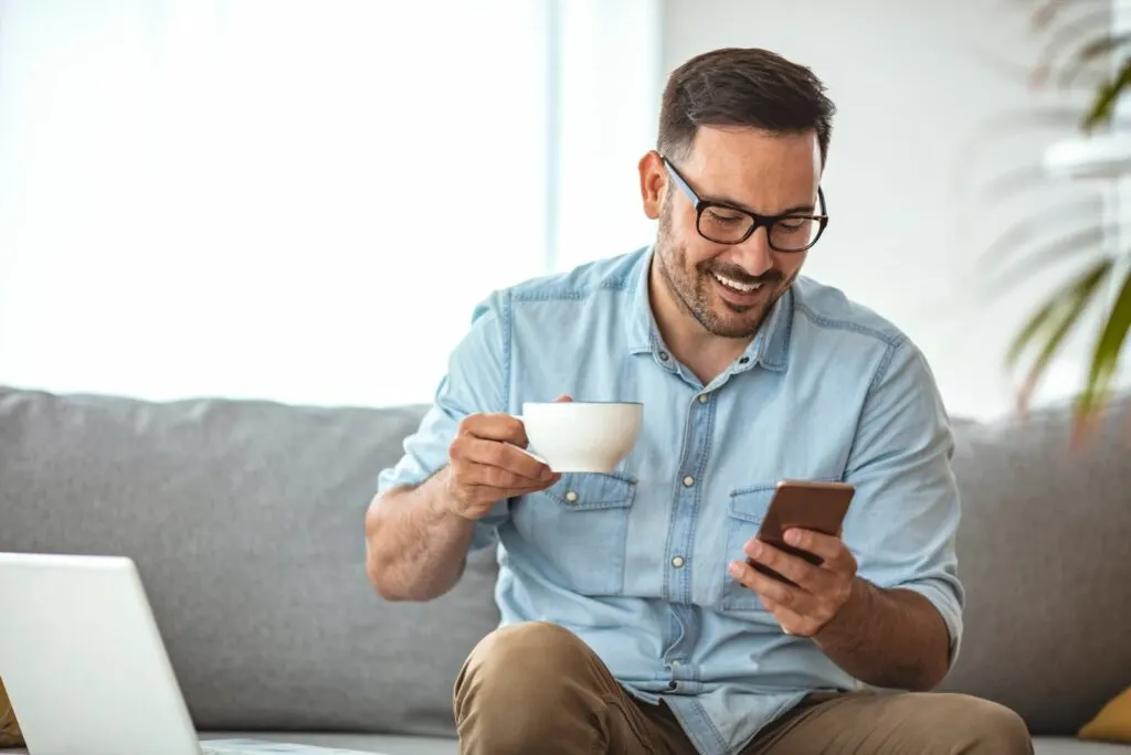 Ein Mann tippt am Telefon, waehrend er Kaffee trinkt