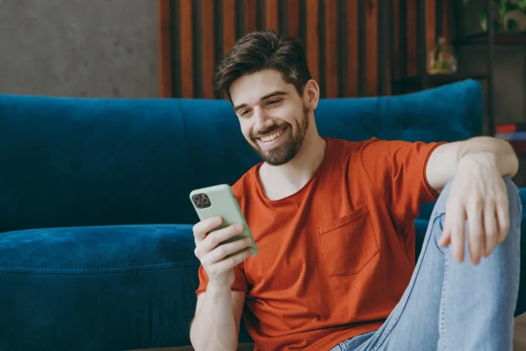 Ein gutaussehender Mann sitzt auf dem Boden und tippt am Telefon