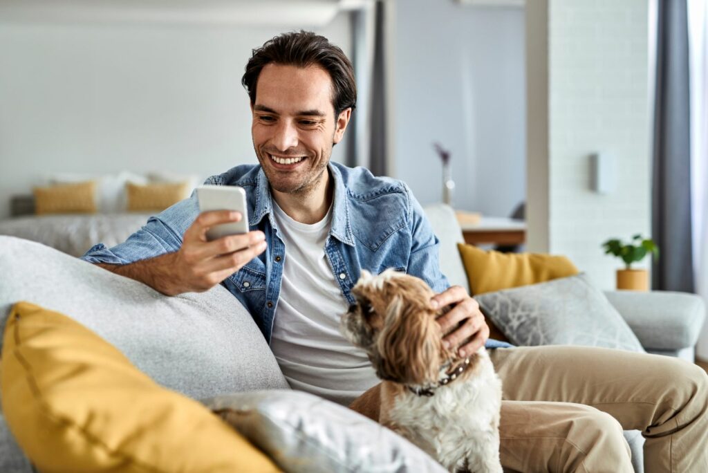 Ein lächelnder Mann mit Hund tippt auf einem Mobiltelefon