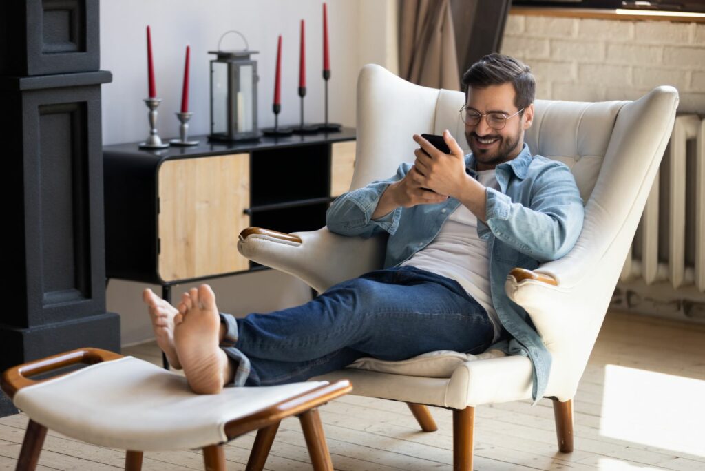 Ein laechelnder Mann sitzt auf einem Stuhl und haelt ein Telefon in der Hand