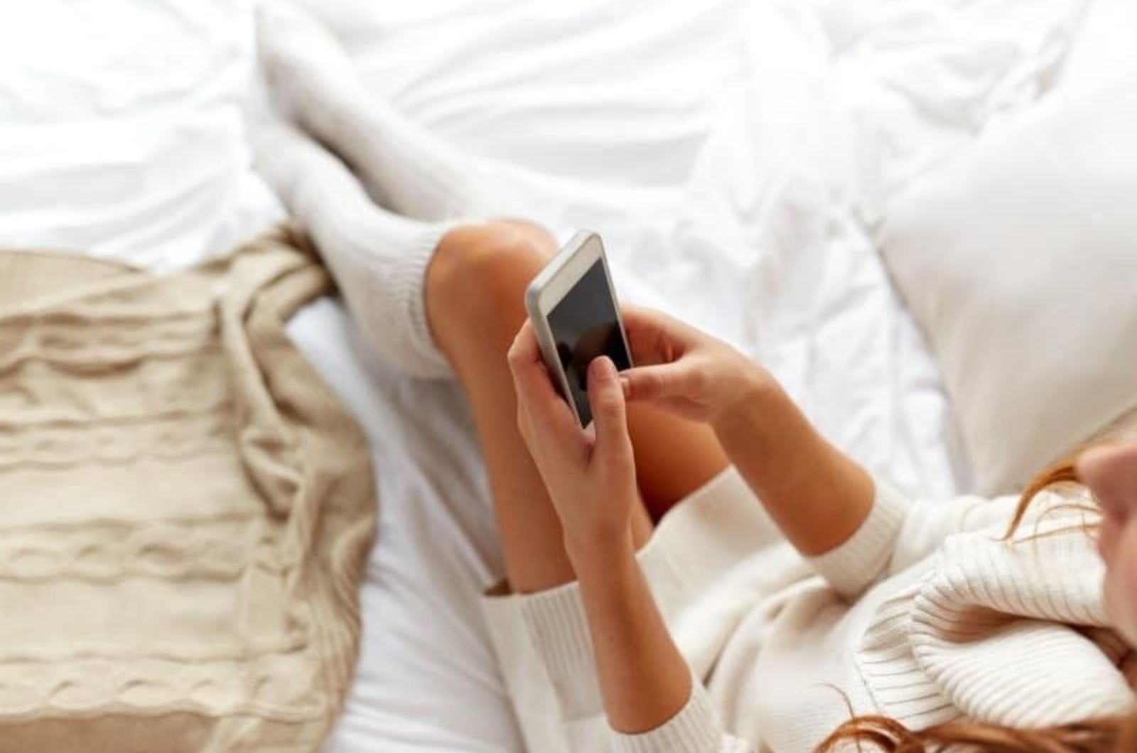 Frau tippt am Telefon im Bett