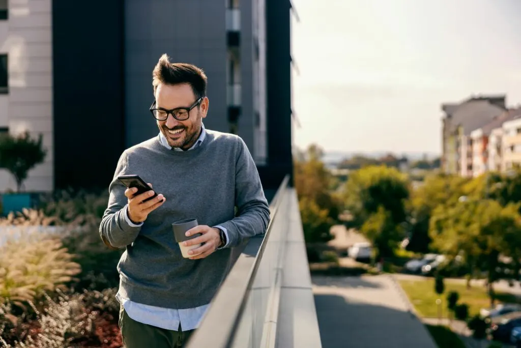 Laechelnder Mann, der draussen steht und auf einem Mobiltelefon tippt