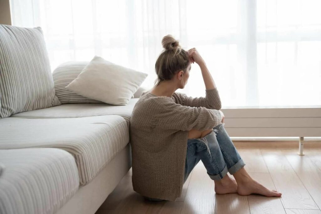 Traurige Frau sitzt auf dem Boden und lehnt sich an die Couch