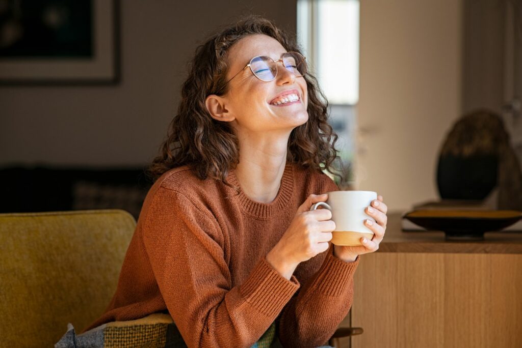 laechelndes Maedchen, das Kaffee auf der Couch trinkt