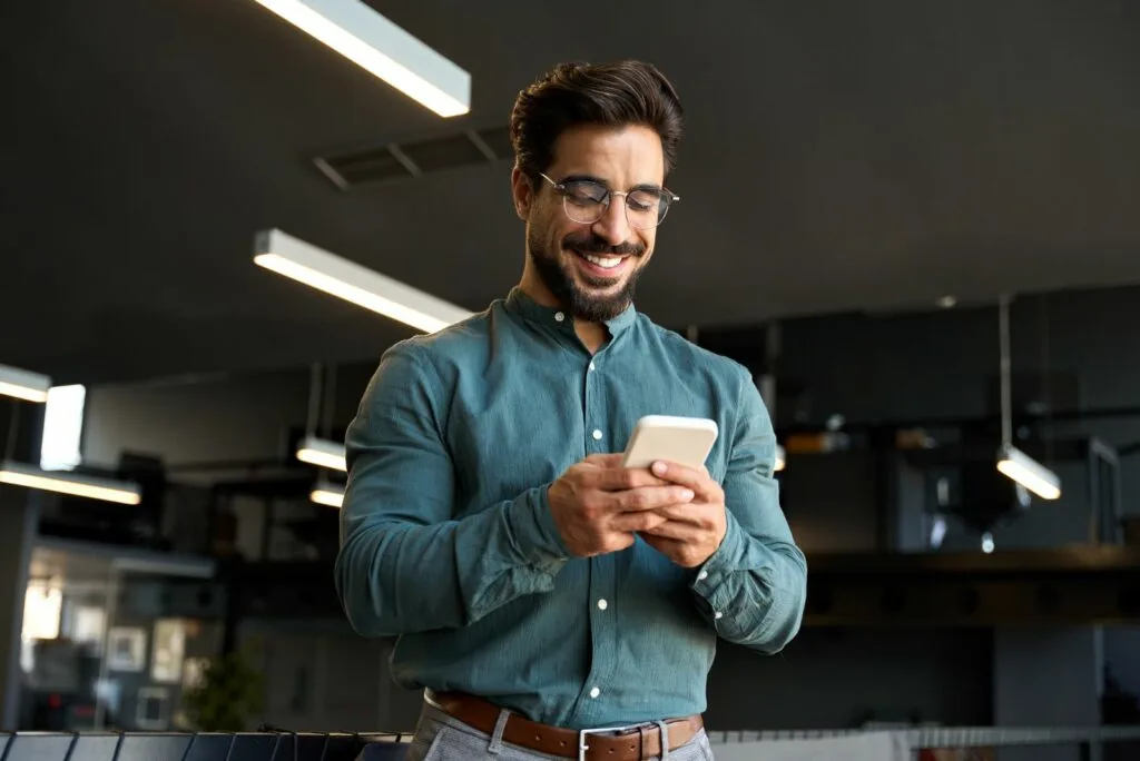 Ein laechelnder Mann hält ein Mobiltelefon in der Hand