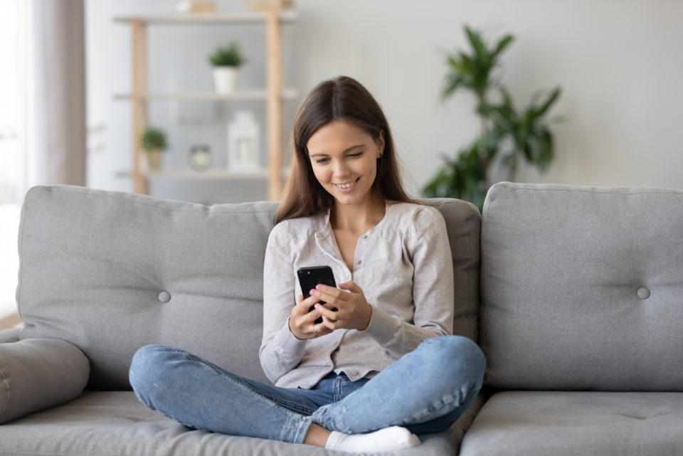 Frau sitzt auf der Couch und schreibt SMS