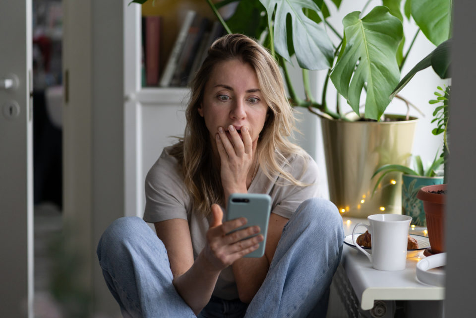 ueberraschte Frau, die auf ihr Telefon schaut