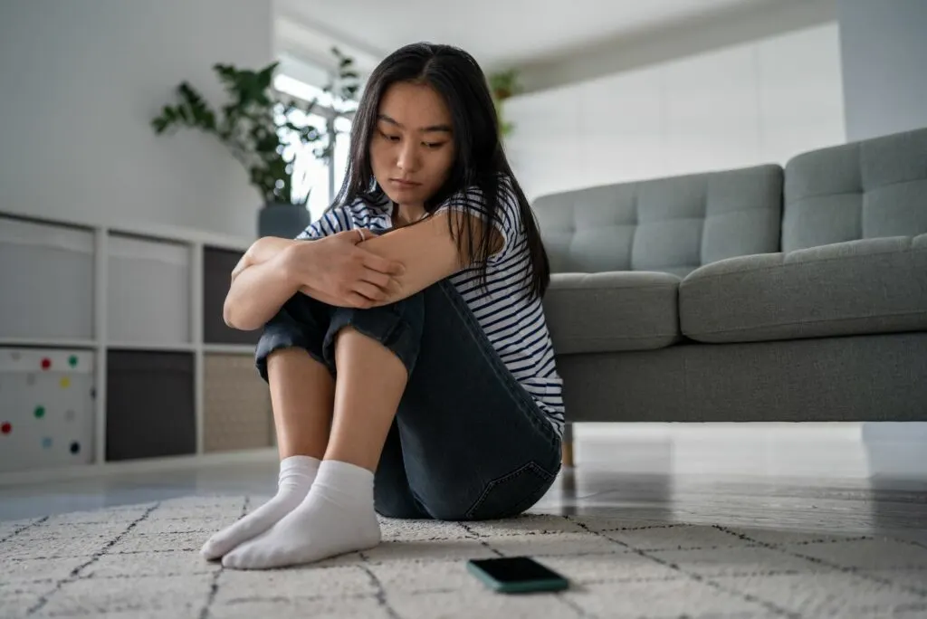 Das Maedchen sitzt auf dem Boden und schaut auf das Mobiltelefon