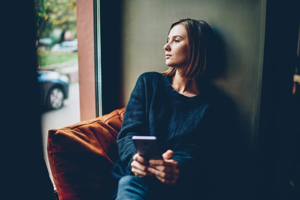 Das Maedchen sitzt auf dem Sofa und haelt ein Mobiltelefon in der Hand