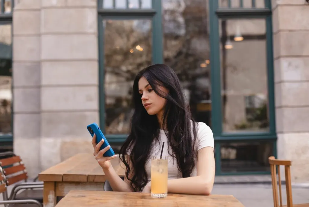 Die Frau sitzt am Tisch und tippt am Telefon