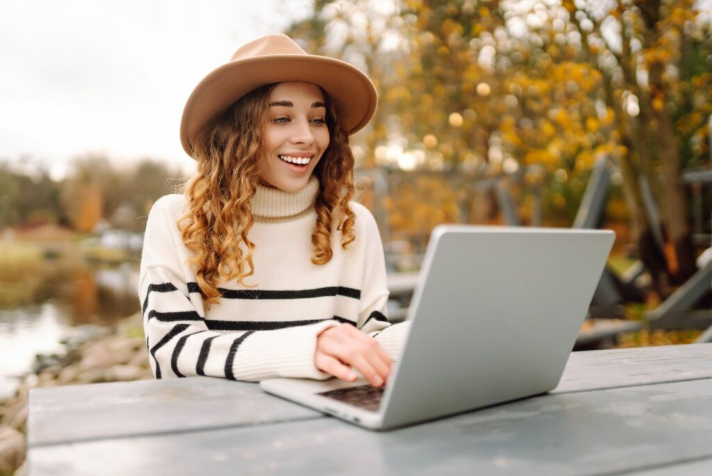 Ein Maedchen sitzt draussen und tippt auf einem Laptop