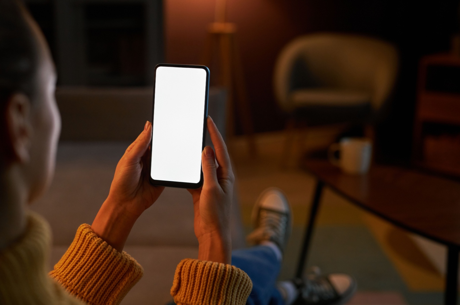 Frau sitzt auf der Couch und haelt ein Telefon