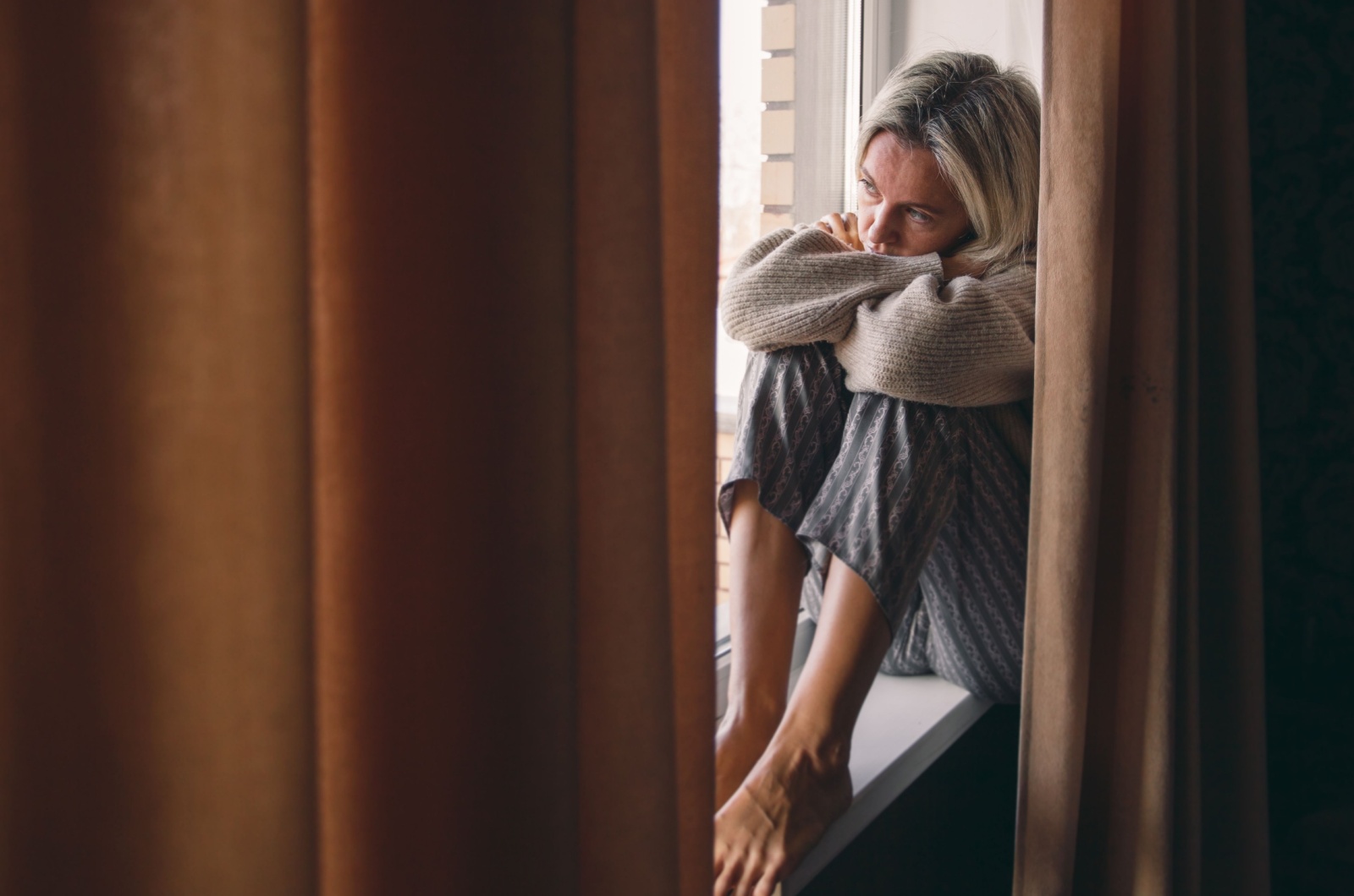 traurige Frau in den Vierzigern sitzt am Fenster