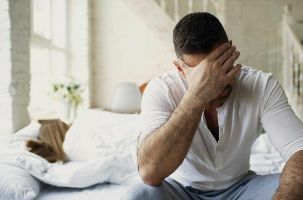 trauriger mann neben frau im bett